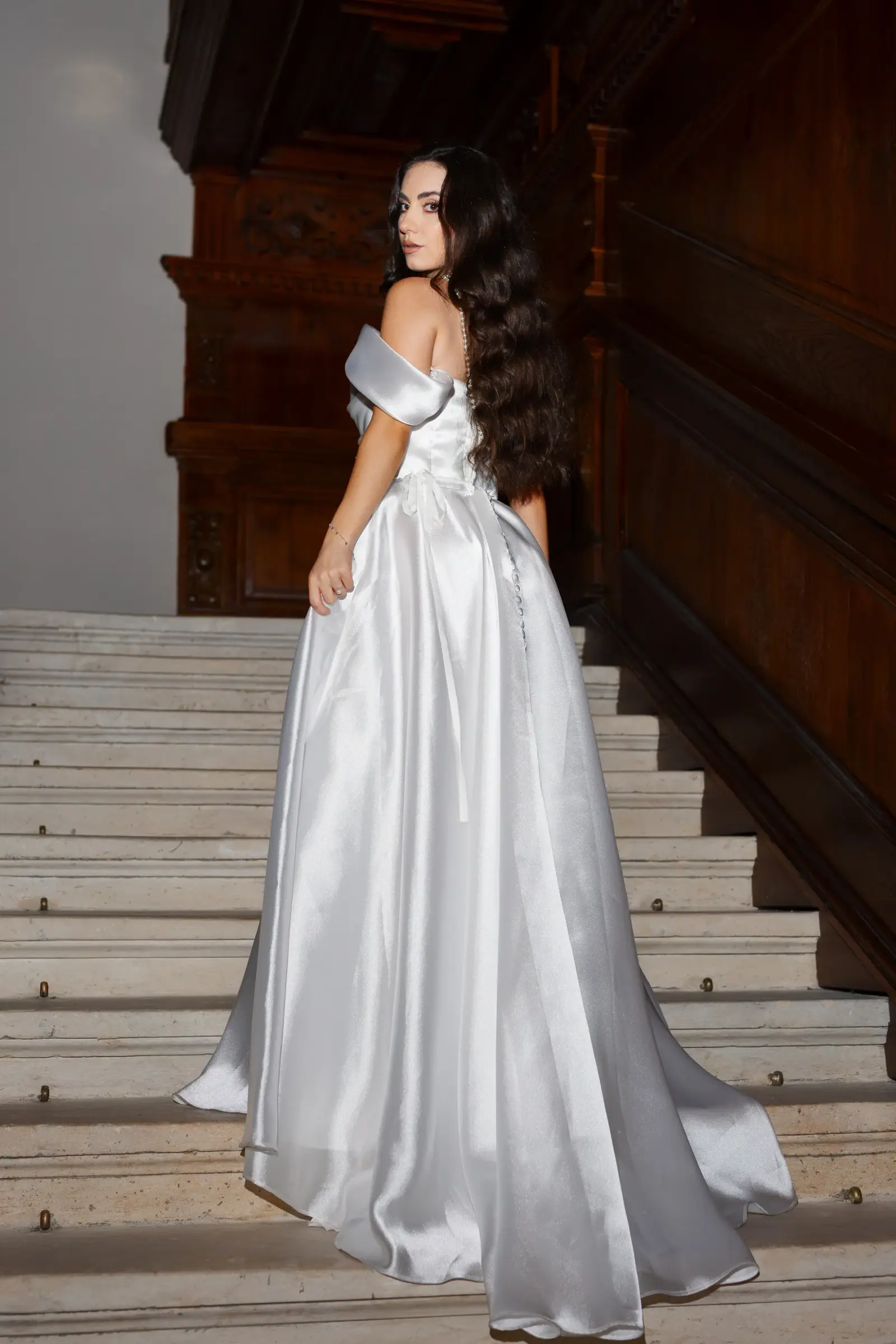 Modelă brunetă prezentând din spate o rochie de mireasă lungă